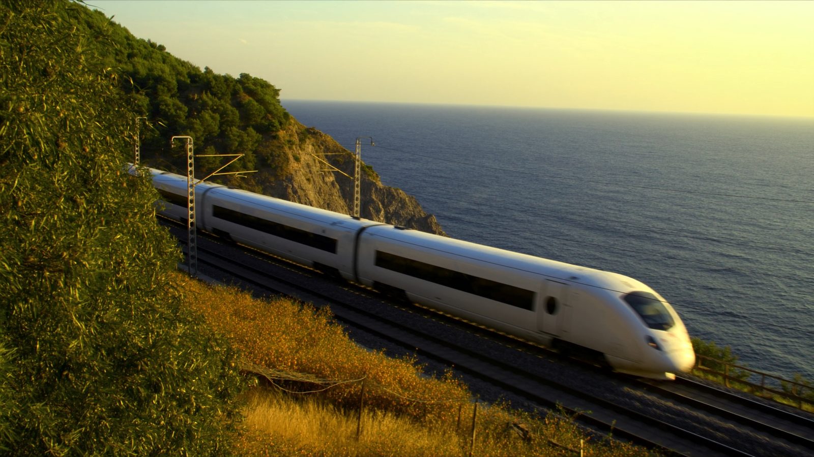 High-speed train speeding along the Spanish Mediterranean coastline at golden hour
