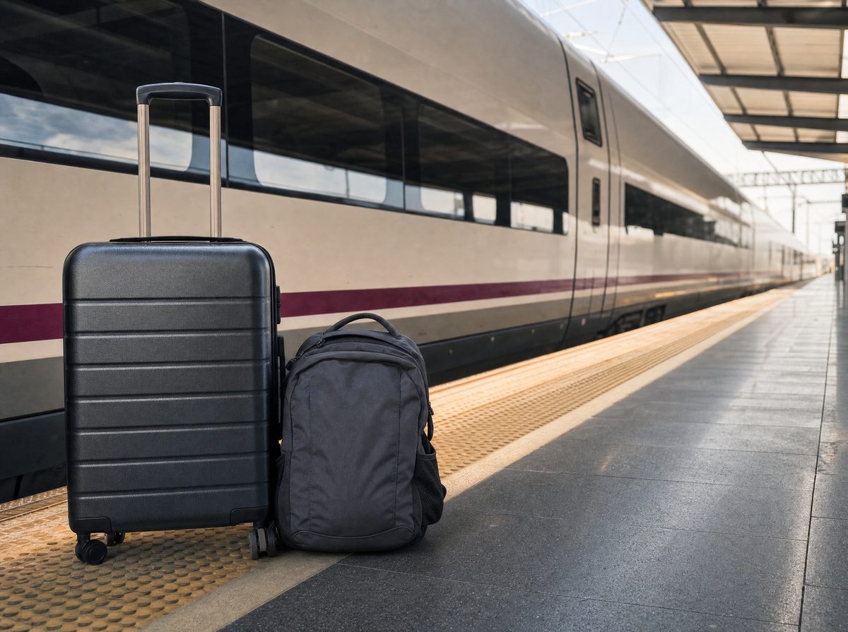 A wheeled suitcase and backpack on a station platform beside a high-speed train